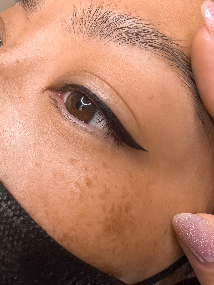 Classic winged eyeliner tattoo on a brown eye, sharp tapered wing