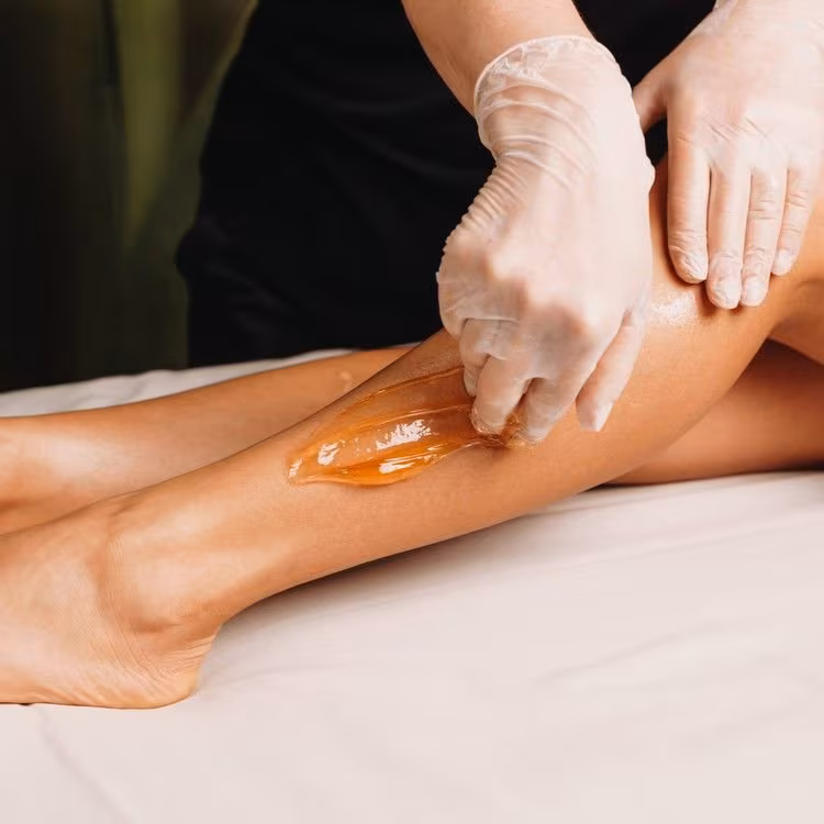 Sugaring paste applied to legs by gloved hands